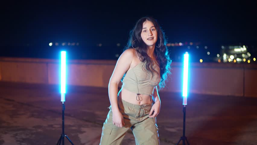 Talented dancer performing a street dance routine under blue neon lights on a rooftop at night