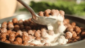 Human hand using a metal spoon to mix cocoa-flavored corn cereal balls with white skim milk in a deep bowl. Crunchy chocolate breakfast ready to eat. Healthy and energizing morning meal - Powered by Shutterstock - Get 15% off with code: PIKWIZARD15