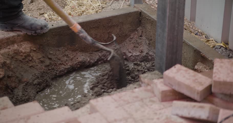 A construction worker mixes cement in a hole at a construction site, preparing the material for building or repair work.