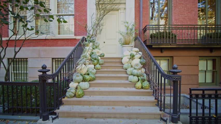 Stoop decorated with pumpkins and squashes in a brownstone in Manhattan, New York City, while pedestrians walk in the street