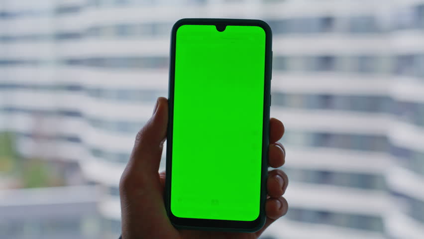 Businessman hand holding greenscreen cellphone near window city view closeup. Unrecognizable freelancer watching chroma key smartphone home. Man manager browsing banking app on mockup mobile phone.