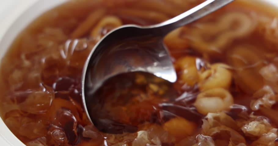 Hand held shake video of Traditional Chinese sweet soup dessert made of longan fruit sugar snow fungus red dates in white dish being served 