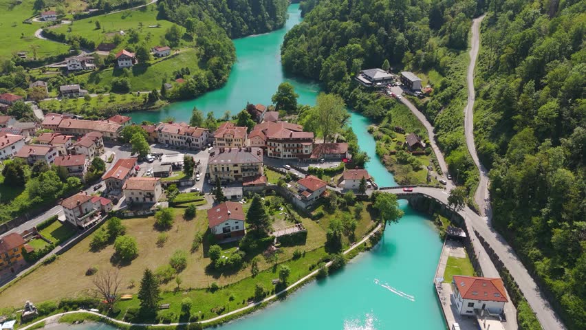 Aerial drone left orbit reveals the iconic bridge of Most na Soči spanning the vibrant turquoise Soča River in Slovenia’s Posočje region, surrounded by lush hills and scenic valley views. Spring time