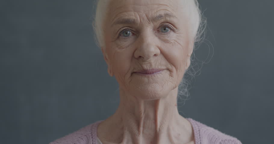 Slow motion portrait of cheerful senior woman smiling looking at camera with happiness on black color background. People and positive emotion concept.