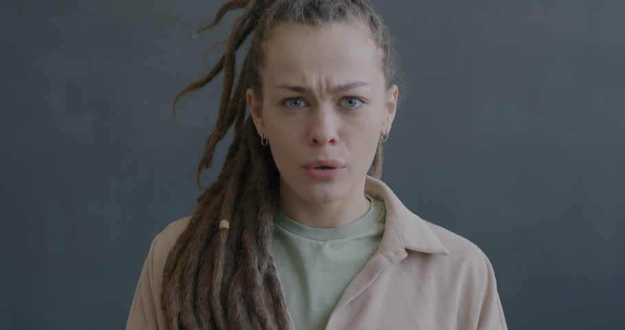 Slow motion portrait of confused and disgusted young woman looking at camera on black background. People and negative emotion concept.
