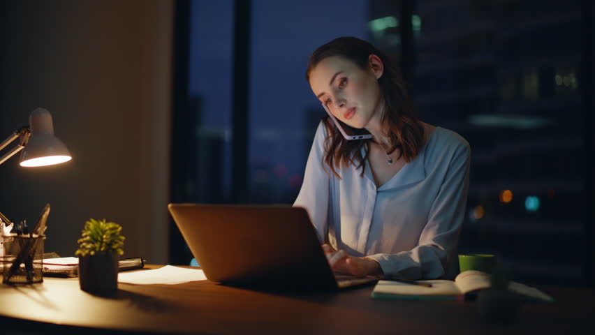 Busy entrepreneur calling cellphone at night office space closeup. Hardworking businesswoman discussing project in phone conversation looking laptop. Serious woman ceo talking smartphone late evening.