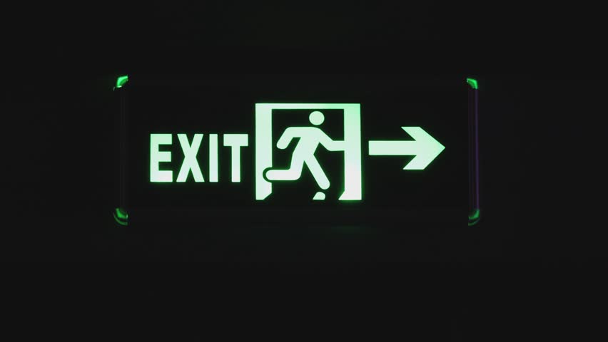 Front view an exit sign glowing in the dark showing the right direction under an emergency with directional arrow.