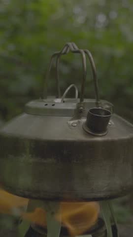 Cooking water over low heat using a Spiritus stove with a tropical forest background.