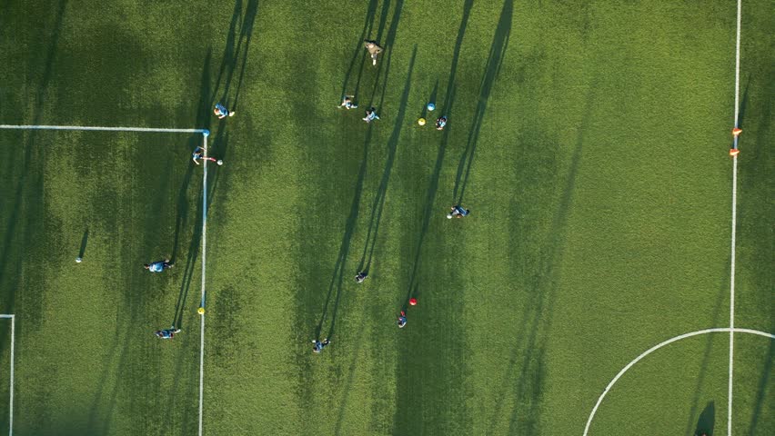 Aerial view of a youth soccer training session on a green field with long shadows cast by players in the late afternoon sun