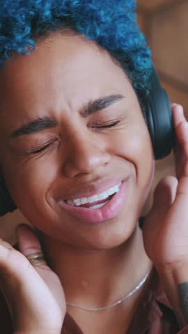 Young African American person enjoys music with headphones, closed eyes capturing every beat. The cozy environment enhances the experience as they lose themselves in the sound, smiling contently.
