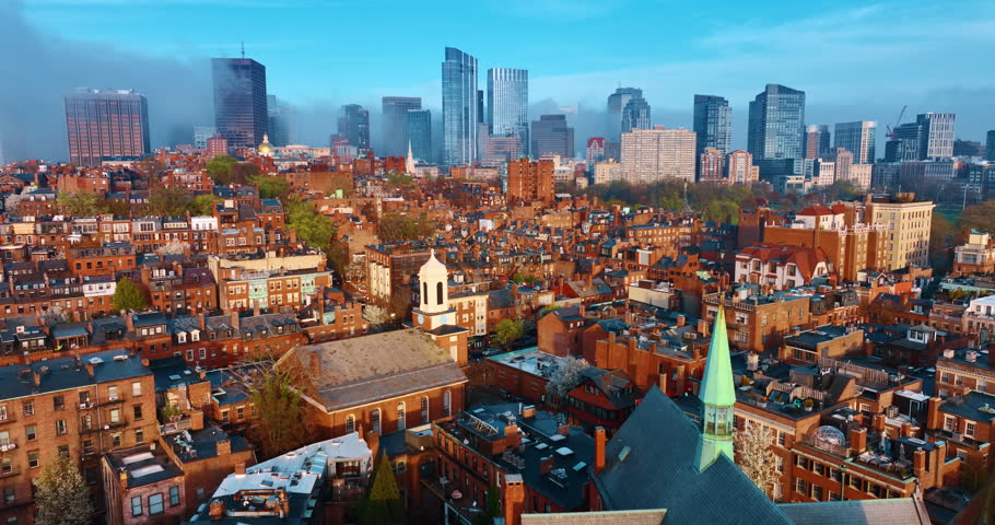 Flying above the bright architecture of Boston. District with multiple old-style buildings with orange facades. Downtown is coated with fog. Aerial perspective.