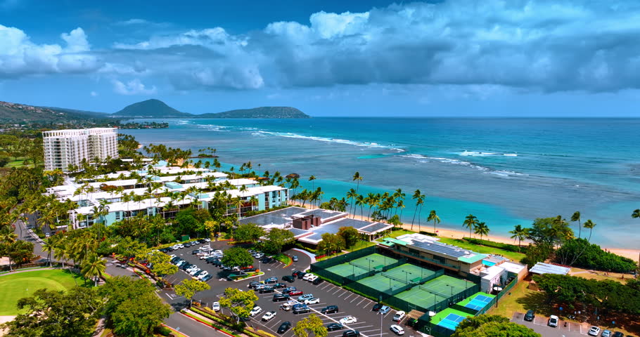 Flying closer to the sandy beach of Honolulu, Hawaii, USA. Foamy waves roll to the coast. Aerial view.