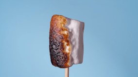 Marshmallow on Stick Burning, Covered with Black Crust, Sugar Bubbling and Smoking. Close-Up Roasting Candy on a Blue Background - Powered by Shutterstock - Get 15% off with code: PIKWIZARD15