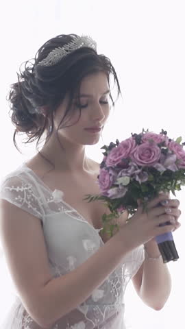 slow motion wonderful young woman in white wedding dress with tiara on brunette hairdress holds purple bouquet