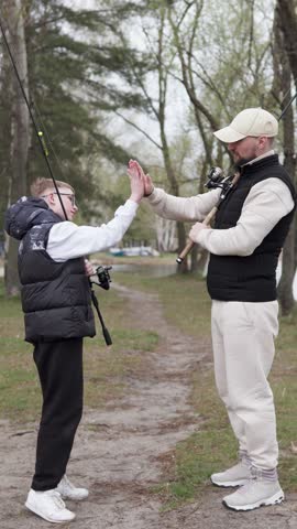 Happy son greeting his father with high five gesture. Father's day with child fishing. Fatherhood concept. Vertical video.