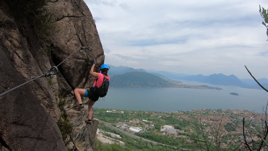 Via Ferrata Picasass, Baveno, Lake Maggiore - Hooked to the cliffside, a woman climber ascends the vertical slab, Lake Maggiore’s horizon blurring behind distant haze and steel rungs.