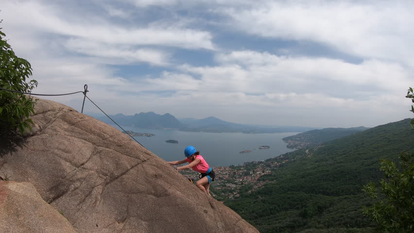 Via Ferrata Picasass, Baveno, Lake Maggiore - Climbing carefully along an exposed slab, the woman adventurer faces gusting winds and open space high above the valley floor and lake.