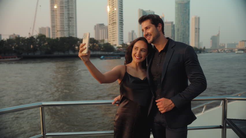 Portrait of affectionate Hispanic couple takes selfie on smartphone on yacht deck. Happy Latin American man and woman make picture for social media sailing motorboat. Sea travel