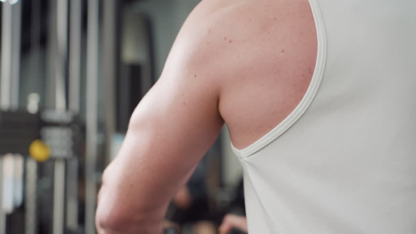 Bodybuilder arm pressing chest press handle on weight machine, muscles contracting under sleeveless shirt as he pushes resistance for intense strength training in gym with focused determination
