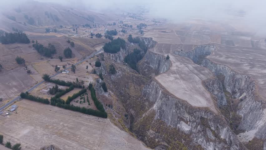 Deep canyon cutting through rugged Ecuador landscape, winding road, nestled village, mountain terrain with expansive fields and geological formations