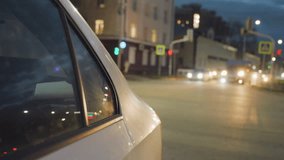 Close up side view of parked vehicle with window reflection showing city lights, while multiple cars with headlights on move along road in background under evening sky with streetlights glowing - Powered by Shutterstock - Get 15% off with code: PIKWIZARD15