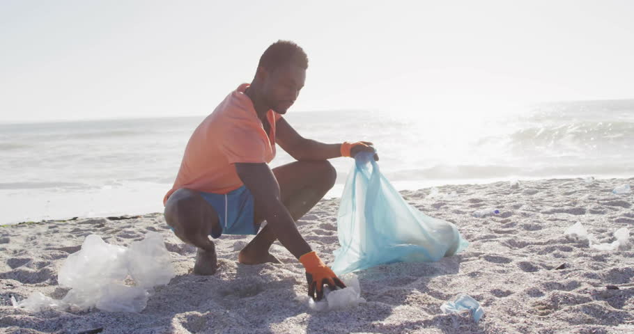 Man volunteering collecting plastic litter on beach for environment, showing floating eco icons. Sustainability, conservation, environmentalism, pollution, eco-friendly, marine, cleanup