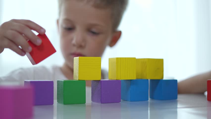 Child building with colorful blocks at home. Focused Child play with block constructor indoors. Home environment encourages creativity. Child hands engaged constructing with blocks. Constructor play.