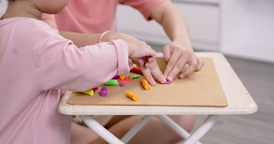 Closeup of preschool girl and Asian single mother hands shaping colorful clay, mother teaching child fine motor control, tactile learning, stimulating creativity, fun relaxed atmosphere in home.