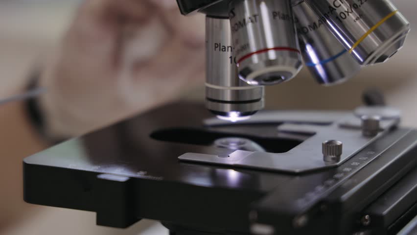Skilled Laboratory assistant conducts research using a microscope, examining scientific sample on illuminated glass slide for detailed medical research. Concept of science, biology, medicine, research