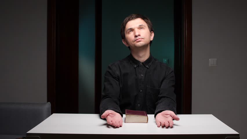 Religious man praying with open hands and holy book on table