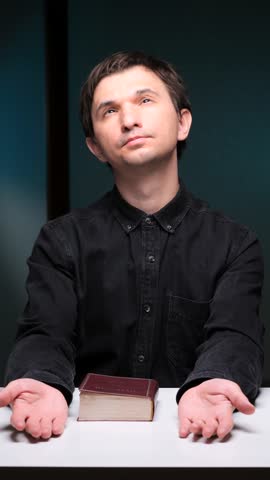 vertical video Religious man praying with open hands and holy book on table