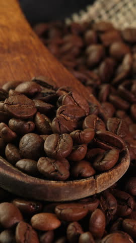 Vertical video roasted coffee beans in spoon side view. Wooden spoon with coffee beans in burlap bag rotates as background for coffee shop, advertising, promo, vending machine