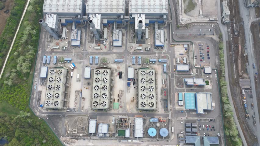 Drone footage of a vast industrial facility surrounded by green fields and a winding river.