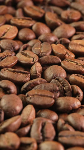 Vertical video roasted coffee beans rotating as background close-up side view. Concept for coffee shop with brown coffee beans rotating as background for advertising, promo, vending machine