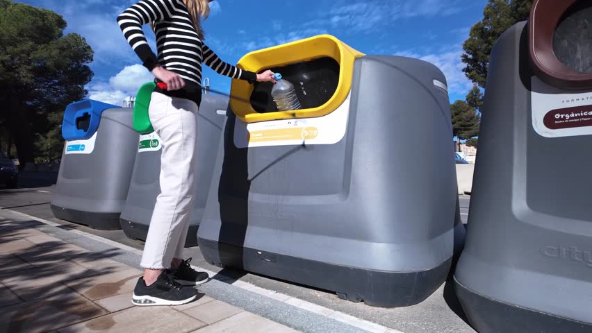 Conscientious person carefully depositing plastic bottles into designated recycling container, supporting sustainable urban waste management practices during bright day