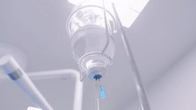 IV fluid bag and tubing drip chamber seen close-up under bright overhead lighting in a clinical hospital setting. - Powered by Shutterstock - Get 15% off with code: PIKWIZARD15