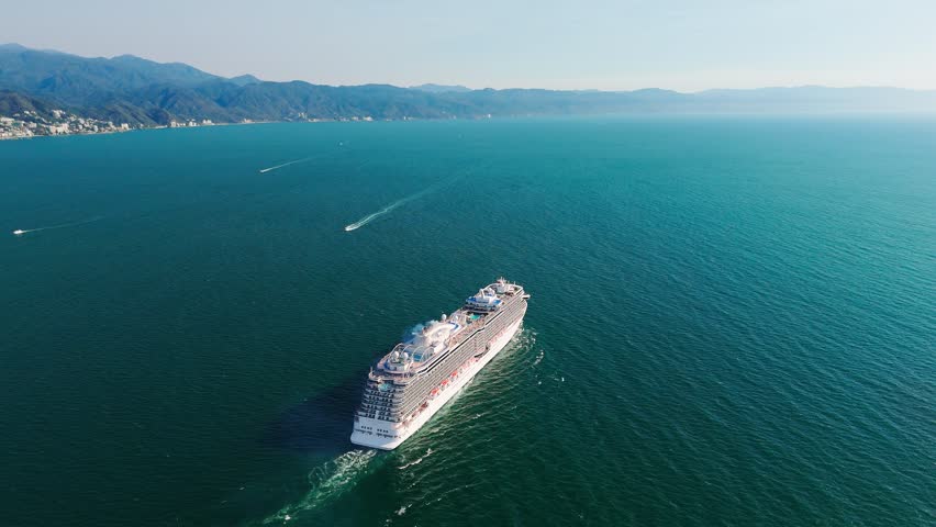 Aerial view of cruise ship sailing away from puerto vallarta, mexico, at sunset, with the city skyline and mountains visible in the distance