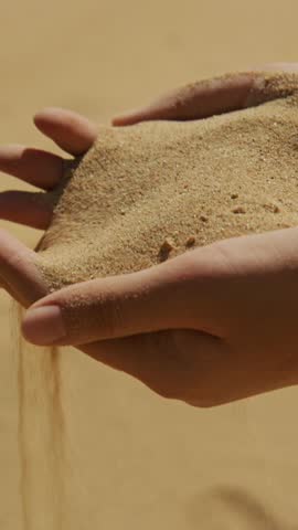 In a tranquil desert setting, hands carefully sift through fine golden sand, letting it cascade down. The sunlight highlights the grains, creating a stunning display of nature's beauty and serenity.