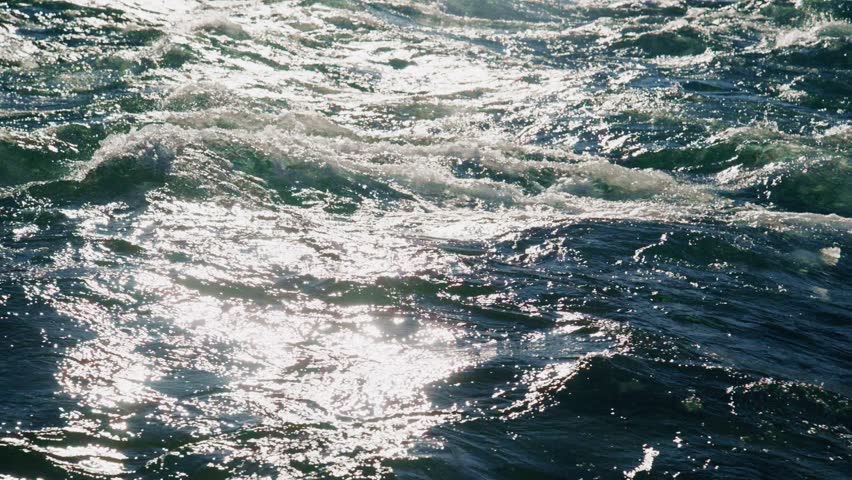 The captivating footage presents stunning visuals of ocean waves undulating rhythmically beneath the bright sunlight, beautifully showcasing shimmering reflections and vibrant textures of the water