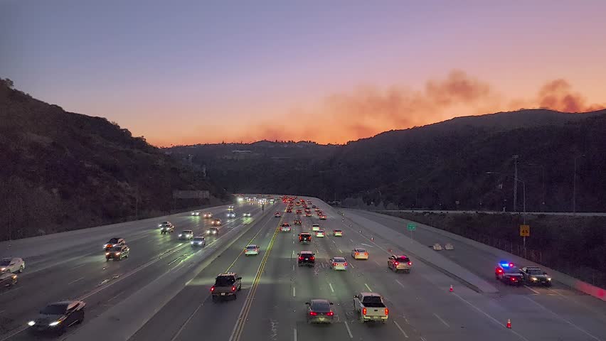 Cars driving on a highway with emergency vehicles and distant wildfires in California