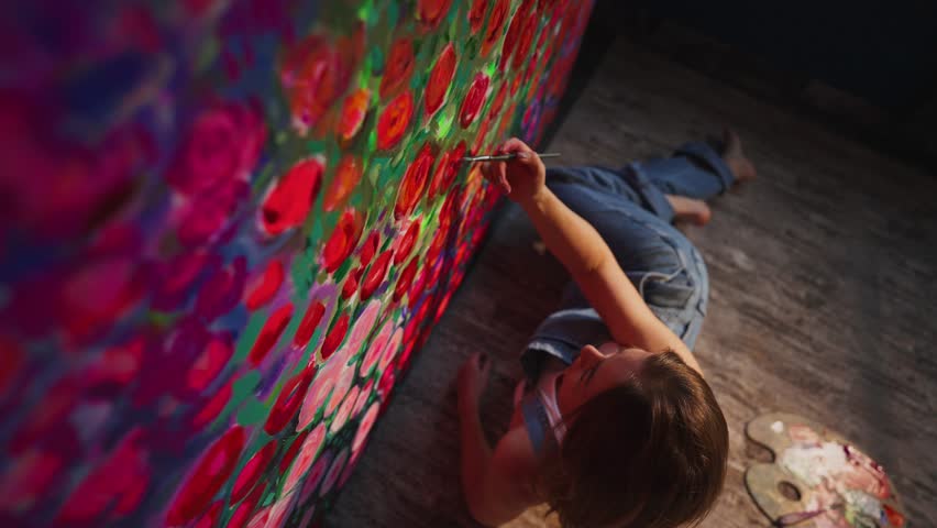 Contemporary artist lying on studio floor, creating large abstract painting with vibrant colors, carefully adding intricate details using small paintbrush while expressing artistic passion