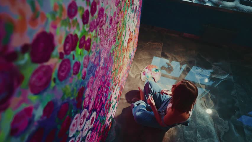 Talented artist sitting on the floor meticulously painting a vibrant and detailed floral mural on a large canvas, adding touches of color to create a stunning piece of art