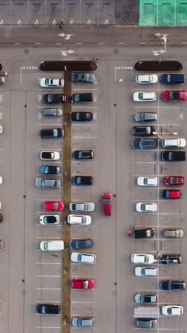 Cars lined up in Riga parking lot during sunset, vertical drone overview framing structure, sedan pulls in and people walk back to cars