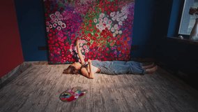 Young female artist lying on hardwood floor, stretching toward vibrant floral painting in sunlit contemporary studio workspace, expressing creative passion through artistic process - Powered by Shutterstock - Get 15% off with code: PIKWIZARD15