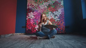 Young artist sitting cross legged on floor, carefully mixing vibrant colors on painter's palette while surrounded by blossoming floral background in creative home studio space - Powered by Shutterstock - Get 15% off with code: PIKWIZARD15