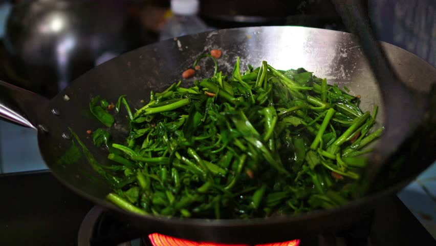 Video footage of a chef making Stir Fried Aquatic Morning Glory in a home kitchen, Thailand.