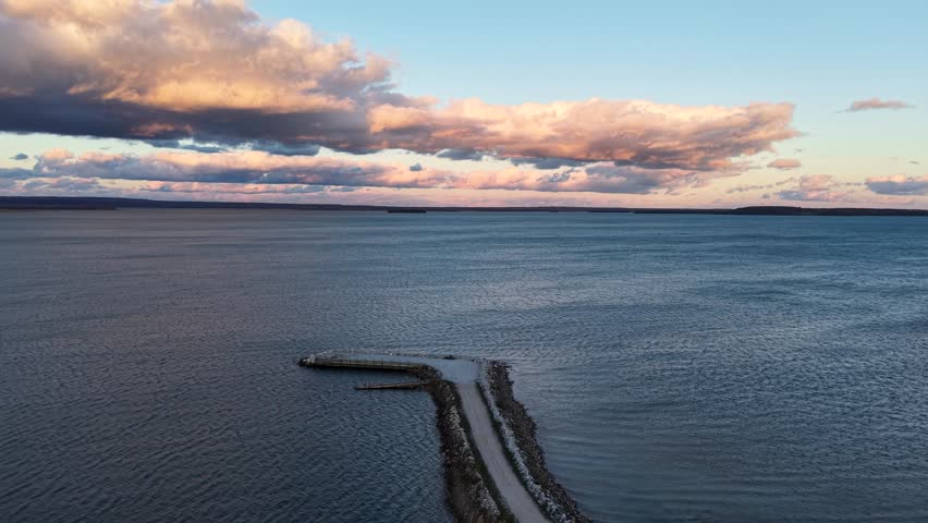 Aerial drone video of a breakwater extending into Lake Superior beneath a glowing sunset sky with dramatic clouds