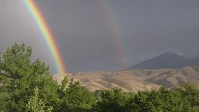 A rare double rainbow lights up the sky over rolling hills and tree silhouettes, filmed in Kyrgyzstan, showing reflection and dispersion of sunlight in droplets. - Powered by Shutterstock - Get 15% off with code: PIKWIZARD15