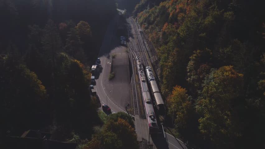 Passenger train winding through vibrant autumn forest, revealing scenic landscape with colorful foliage and mountain valley backdrop