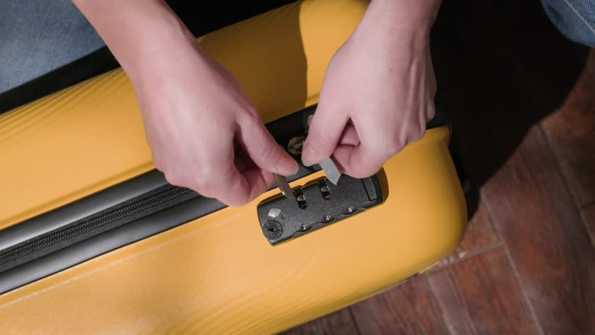 Woman hands closing zipper on yellow travel suitcase in room close-up top view. Concept of packing luggage for journey.